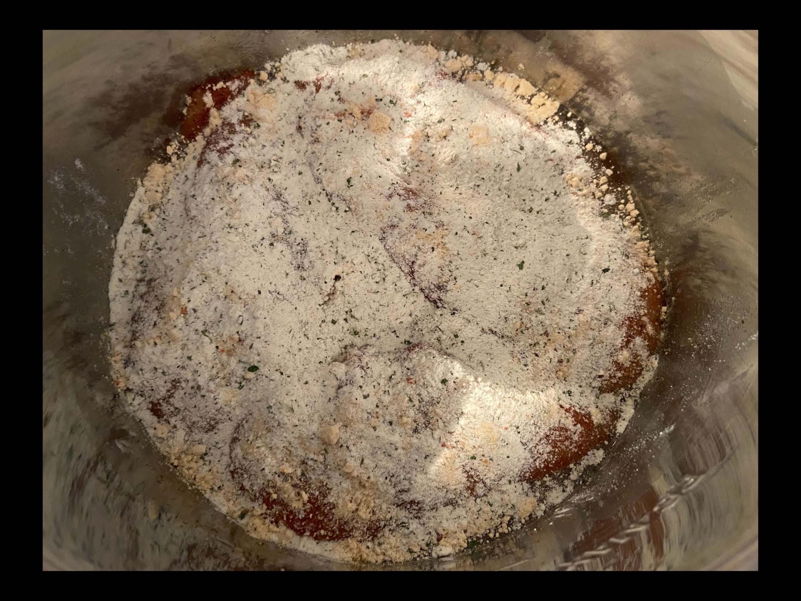 An instant pot filled with raw chicken breast covered with dry ranch dressing packet, dry itallian seasoning packet, and dry chicken gravy packet.