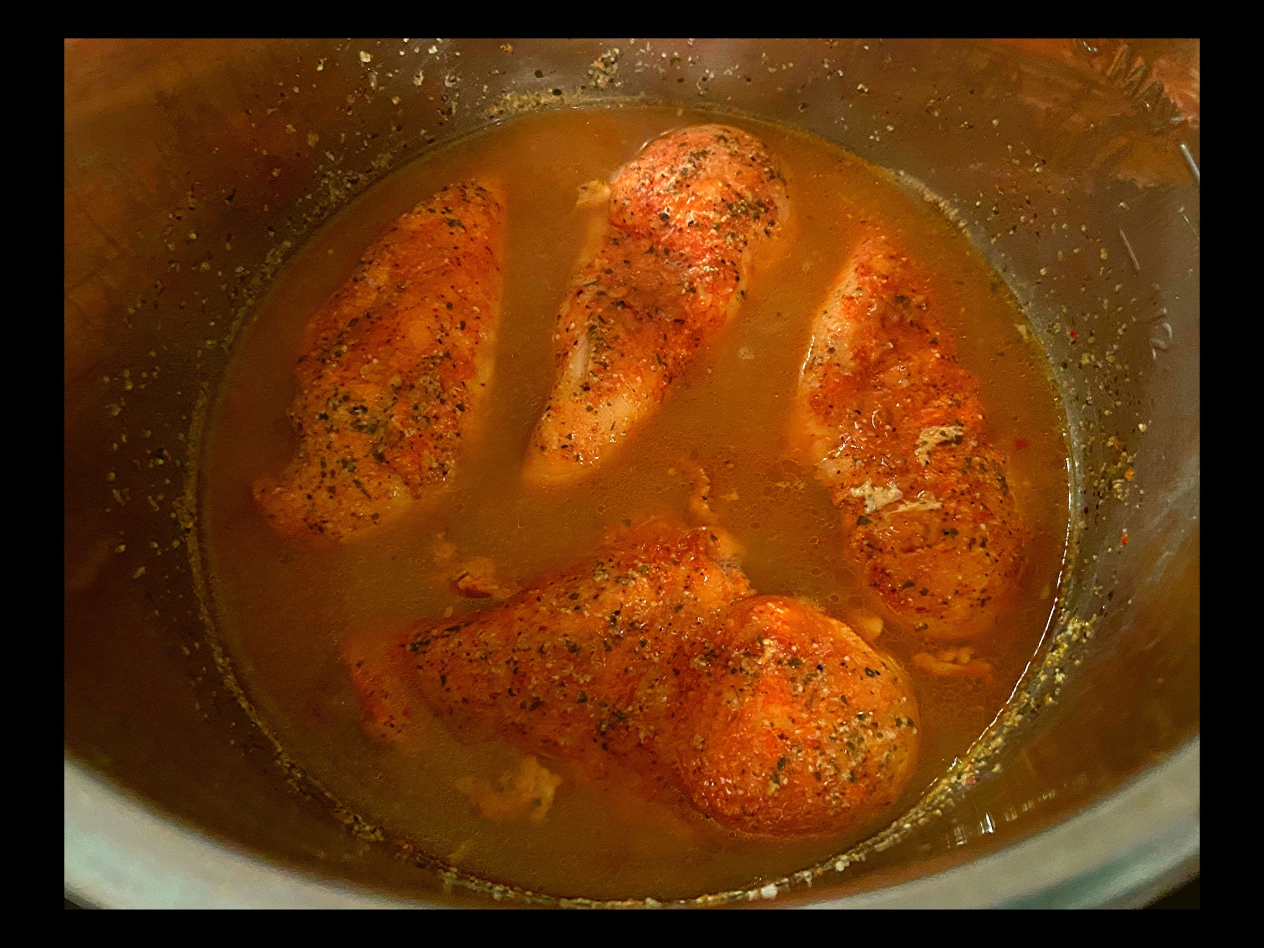 An instant pot filled with raw chicken breast covered with dry ranch dressing packet, dry itallian seasoning packet, and dry chicken gravy packet.